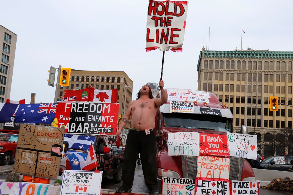 Une personne tient une pancarte devant des camions bloquant une rue du centre-ville alors que les camionneurs et leurs partisans continuent de protester contre les mandats pour un vaccin contre le coronavirus (COVID-19) à Ottawa, Ontario, Canada.